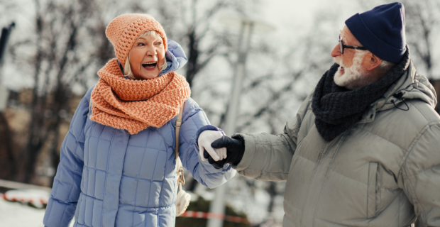 Two people dressed in heavy winter coats, scarves, and gloves walking hand in hand on a snowy path, illustrating a winter safety guide.