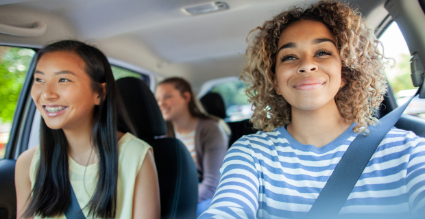 Young person driving a car with two passengers, all wearing seatbelts, travelling together on a sunny day.