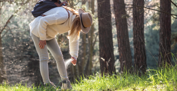 A woman bends down to apply tick repellent spray to her ankles during a walk in the forest.