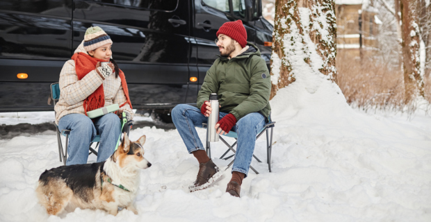 A couple sitting in chairs on a winter campsite with their dog in front of their motorhome.  