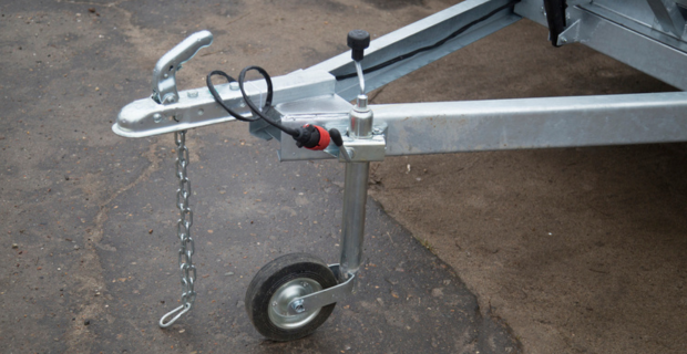 A metal trailer hitch covered in a weather proof grey tarp. In the background is an empty trailer hitch. Behind them is a house with brick and blue trim. A wooded yard is in the background