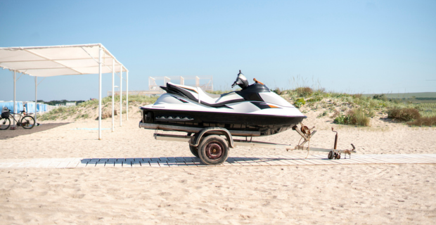 A personal watercraft is on a trailer sitting on a walkway near a beach.   
