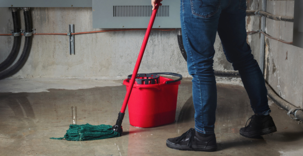 Person mopping standing water in a flooded basement, illustrating the importance of coverage for water damage.