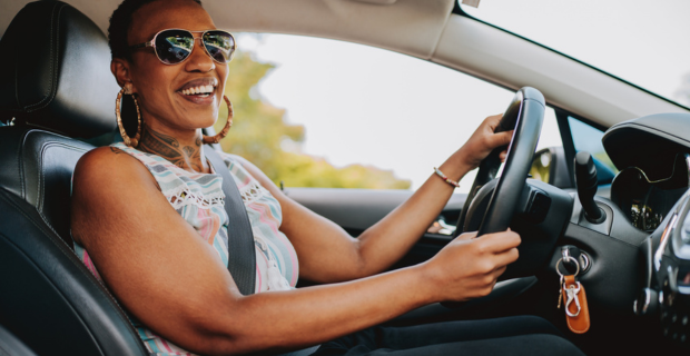 A happy person saving on car maintenance inside their vehicle driving and wearing a sleeveless shirt. 